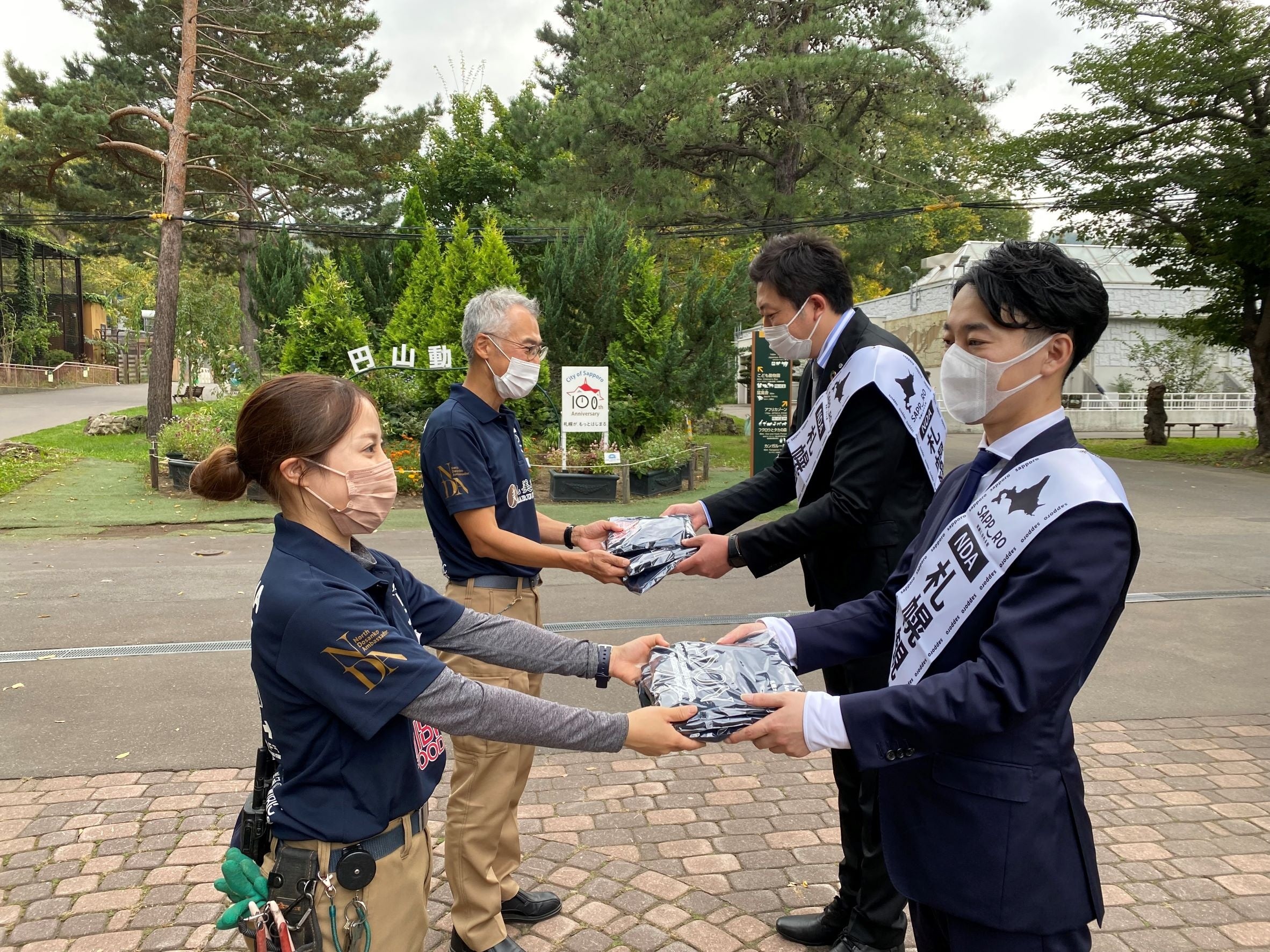 アイビック食品株式会社代表取締役社長牧野克彦氏らより札幌市円山動物園神園長と札幌市円山動物園ゾウ舎担当野村友美さんに手渡されるユニフォーム